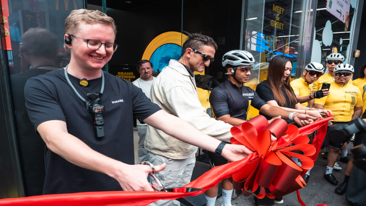 Insta360 Co-founder Max Richter cuts the ribbon at the Times Square flagship grand opening, joined by Casey Neistat and cyclists in branded yellow jerseys outside the storefront at 1515 Broadway.