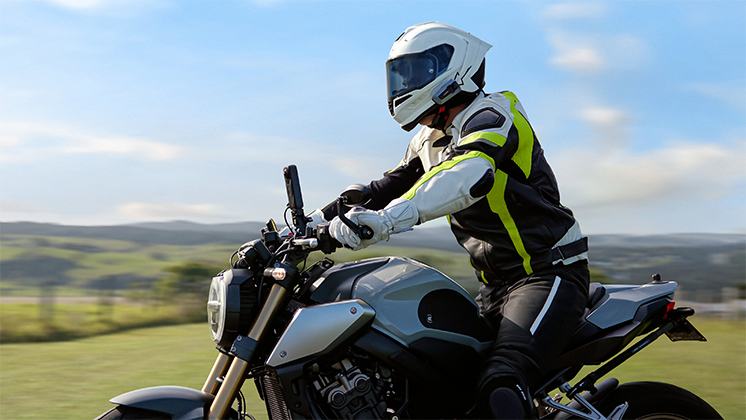 A motorcyclist riding a naked bike on a scenic road with an Insta360 camera mounted to the handlebars.