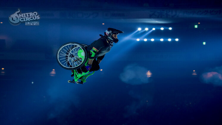Aaron “Wheelz” Fotheringham mid-air on a green wheelchair at Nitro Circus.