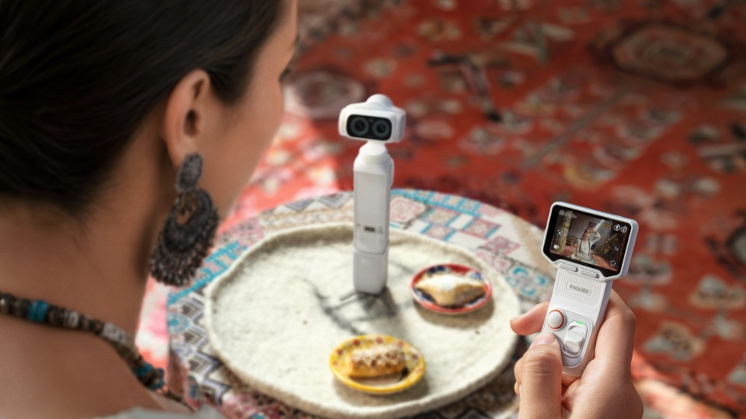Insta360 Unveils Luna Ultra Dual-Lens 8K Gimbal Camera 4 Image displaying a woman in a cafe holding the detachable 2" OLED touchscreen of the Stellar White Insta360 Luna Ultra, allowing her to frame a selfie shot of herself.