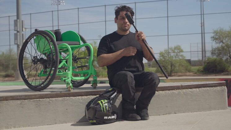 Aaron “Wheelz” Fotheringham sitting on a step holding Insta360 X5, with his green wheelchair in the background.