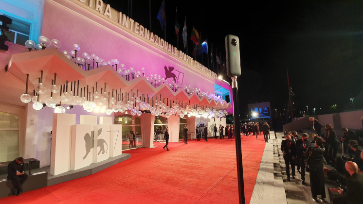 An Insta360 ONE X camera on an extended pole overlooking the illuminated red carpet at the Venice Film Festival at night.