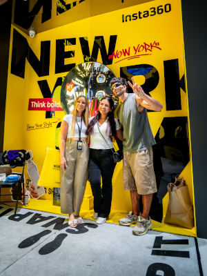 Jesse Wellens, Jen Smith, and an attendee pose in front of the Insta360 "Think bold." New York graffiti wall at the Times Square flagship opening, with a giant inflatable 360° camera balloon between them.