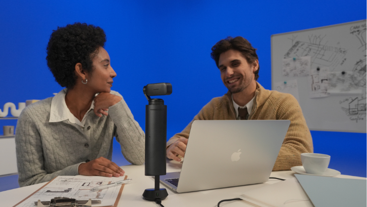Two professionals collaborating at a desk with Insta360 WaveLink Pro speakerphone and laptop in a modern hybrid workspace setup.